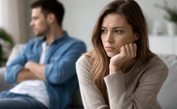 Woman looking sad and thoughtful while her ex boyfriend sits in the background appearing distant and angry after a breakup.