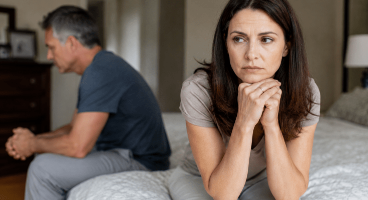 Worried married couple sitting apart on a bed during a relationship crisis, illustrating emotional distance, marriage problems, and separation anxiety.